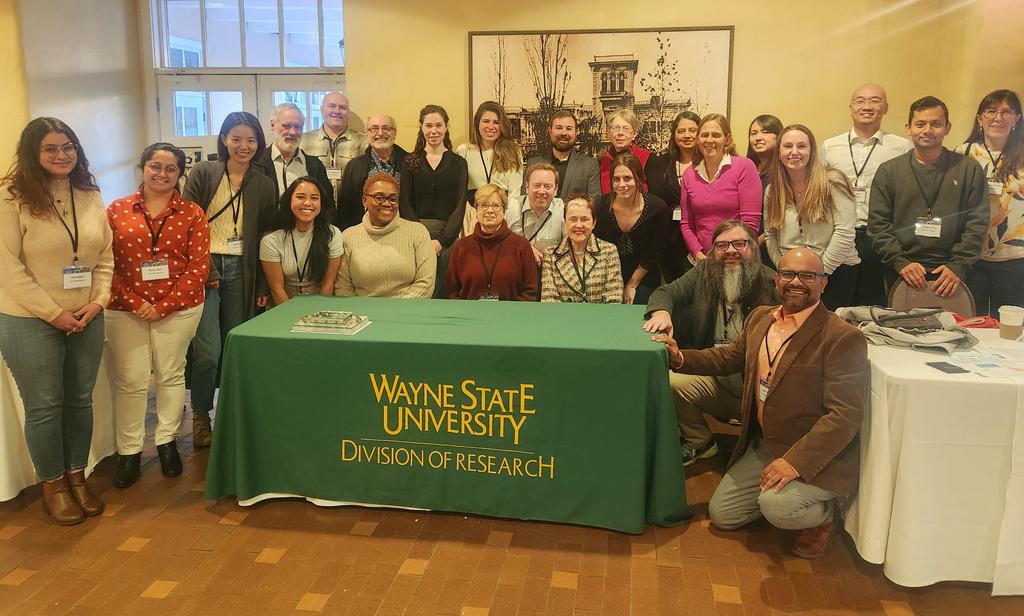 Large group picture of individuals involved in CLEAR with green table in center that displays text Wayne State University Division of Research in yellow